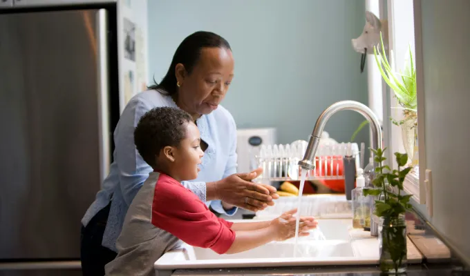 Photo of an African American grandma teaching her young grandson how to wash his hands.