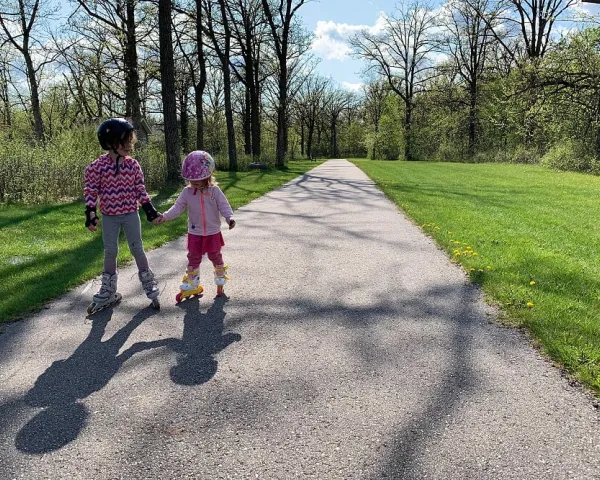 Two little girls roller skating down a trail