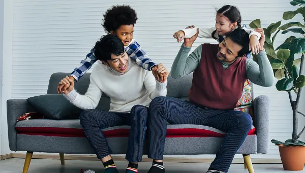 Photo of a male same-sex couple sitting on a couch, with their two young children